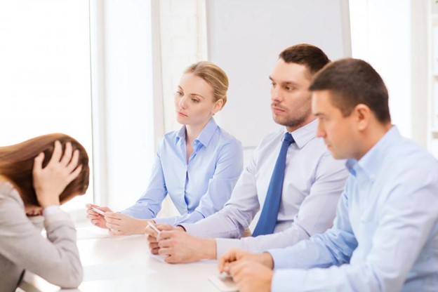 An employee sitting with her managers and holding her head in distress as she gets fired from her job